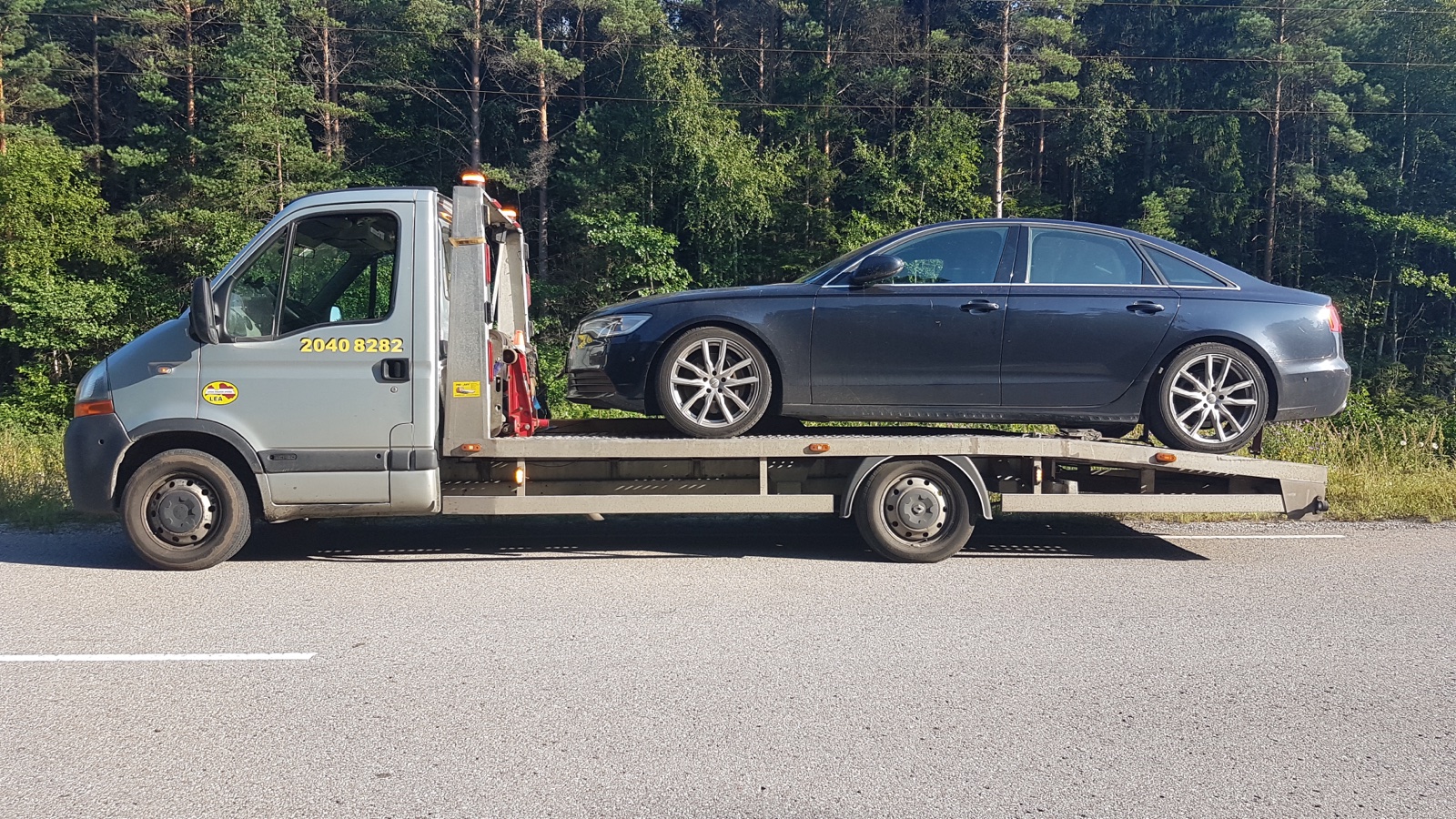 Autoevakuators transportē pārkarsušu auto saulainā vasaras dienā ceļa malā